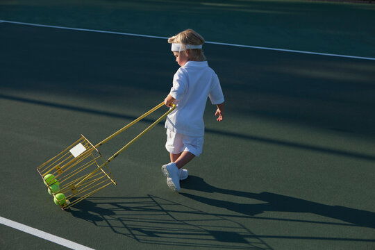 Boy (2-3) pulling basket with tennis balls