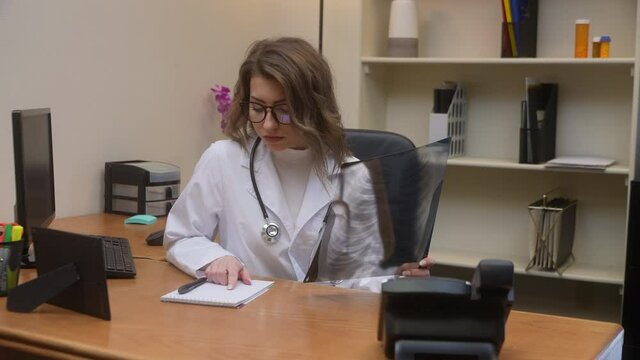 Pretty female doctor examines chest x-ray and makes phone call regarding something of concern