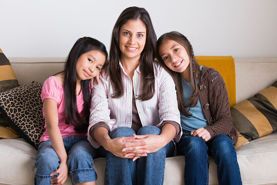 Portrait of happy mother with two daughters (8-9, 10-11) sitting on sofa