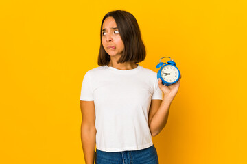 Young hispanic woman holding a megaphone confused, feels doubtful and unsure.