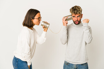Young hispanic friends talking through a tin can system showing fist to camera, aggressive facial expression.