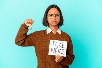 Young hispanic mixed race woman holding a fake news placard showing a dislike gesture, thumbs down....