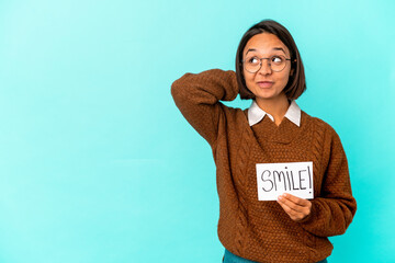 Young hispanic mixed race woman holding a smile note touching back of head, thinking and making a choice.