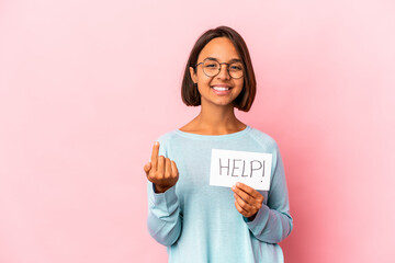 Young hispanic mixed race woman holding a help poster pointing with finger at you as if inviting come closer.