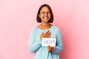 Young hispanic mixed race woman holding a help poster laughs out loudly keeping hand on chest.