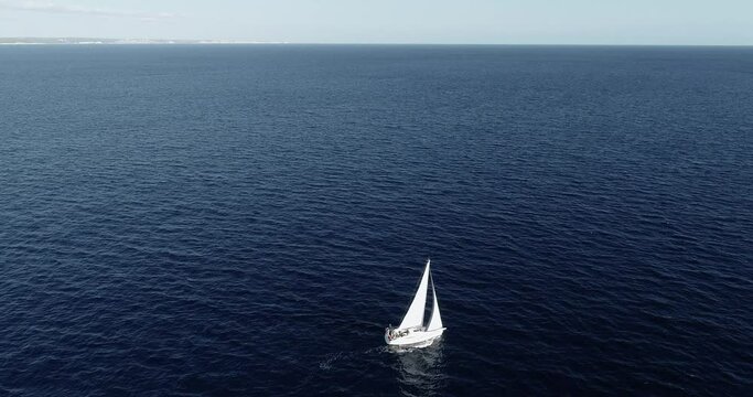 Sailboat sailing in the middle of the Mediterranean Sea under the blue sky. Perfect for leisure activity in travel and holidays - close view with a drone 4K