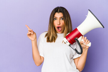 Young indian woman holding a megaphone isolated pointing to the side