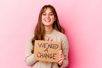 Young caucasian woman holding a We need a change placard isolated laughs out loudly keeping hand on chest.