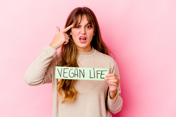 Young caucasian woman holding a vegan life placard isolated showing a disappointment gesture with...