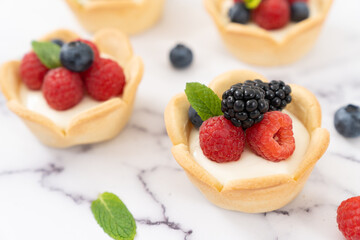 Delicious pastry mini fruit cream cheese pies or tart cakes with fresh raspberry, blueberry and blackberry