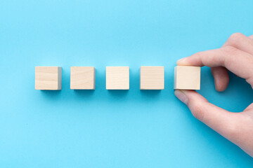 Hand holding a row of five blank wooden cubes on a blue background in a conceptual image, ready for your text.