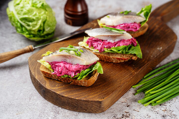Three herring sandwiches with beet and green salad leaves on wooden board. Close up. Omega 3 fats...