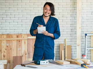 Good looking Asian carpenter wearing coverall dress working for DIY jobs in carpenter room with...
