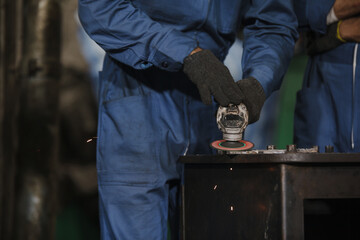Young manual worker using grinder on metal in factory. Worker grinding in a workshop. Heavy industry factory, metalwork