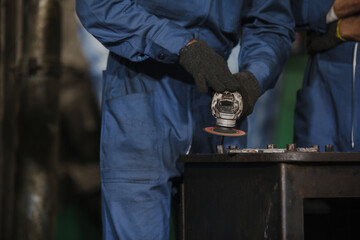 Young manual worker using grinder on metal in factory. Worker grinding in a workshop. Heavy industry factory, metalwork
