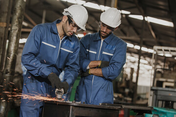 Young manual worker using grinder on metal in factory. Worker grinding in a workshop. Heavy industry factory, metalwork