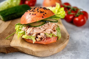 Delicious salmon burger with pink bun on a wooden board. Healthy seafood concept. Omega 3 fats. Brain food