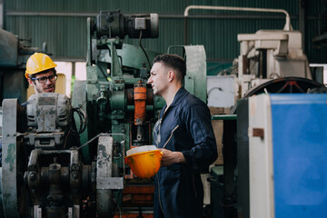 Two workers at an industrial. technician engineer checking process on notebook to machinery in factory. workers using machine equipment in factory