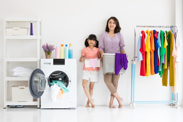asian mother and cute daughter holding basket of clothes standing and smile between a washing...