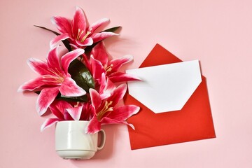 Happy Mother's Day, Women's Day, Valentine's Day or Birthday. White cup with lily flowers and red envelope on a pink background. minimalism. creative. Greeting card. Flat lay, copy space.