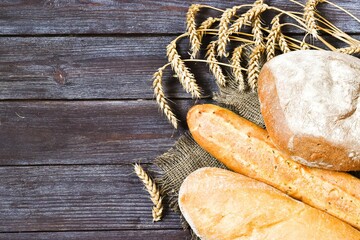 Fresh bread and wheat ears on a wooden table. Copy space, flat lay.