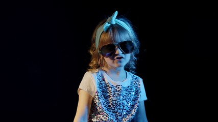 Close-up portrait of young sensual playful blond girl in bright blue neon rays light singing on black background. Stylish trendy child kid at disco party cyberpunk club making faces, fooling around