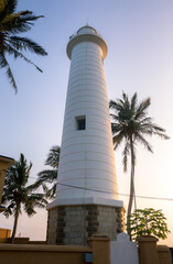 Lighthouse glowing in the evening sunlight, Galle Dutch fort, Palm trees, and the cost scenic landscape photograph. Sri Lanka's oldest light station and tourist attraction and a world heritage site.