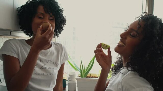 Two Beautiful black women with curly hair holding kiwis in their hands and smiling
