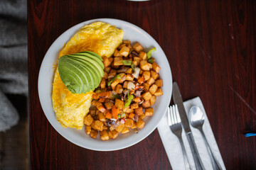 Omelette, roasted potatoes and avocado slices on a white plate