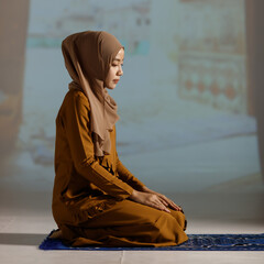 Portrait of a young and beautiful Muslim woman in red hijab dress sitting and meditating in the mosque.