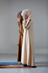 Two young Asian Muslim women in hijab dress standing and praying together. Idea for religious ritual and calm of mind