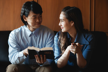 Asian man sitting teaching a Bible prayer to a Christian woman. As a confession of sins and...