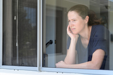 Fototapeta na wymiar Upset middle aged adult woman (age 30-40) looking through home window. Real people. Copy space