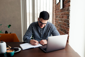 Fototapeta premium Man working at the laptop with a cup of coffee at home. Blurred background