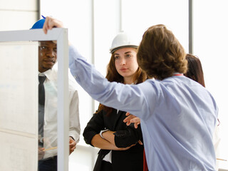 A man African American  and Caucasians as a group Meeting on construction operations. There is a Transparent board clear work plan. Wearing helmet equipment. Concept men Caucasian Meeting leadership.