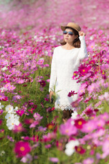 Beautiful Asian woman wearing white dress in cosmos flowers field blooming in the garden.