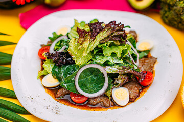 warm salad with meat, tomatoes and egg on a decorated table