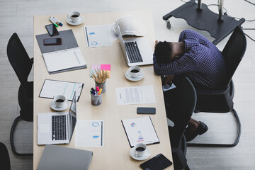 A man African American looking down on the smartphone While waiting for the meeting In the meeting room in the office there is a laptop, coffee and presentation plan.