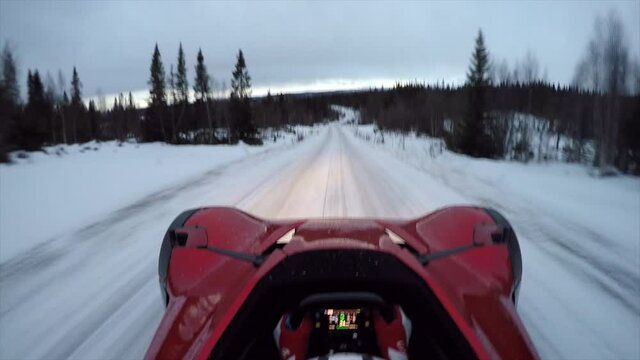 Single seater BAC MONO driving down snow cover ice road in Sweden after the sun has set. Exiting over the drivers head view showing car control skill.