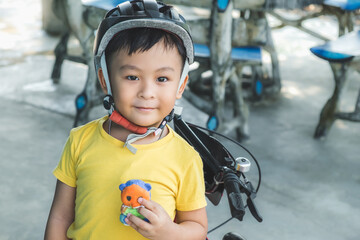 Happy kid Asian boy having fun on road ride bicycle in city. Active little child smiling while wearing helmet for bike sport outside. Young small biker playing cycle in park. Safety exercise concept.