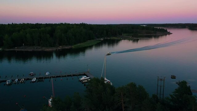 Aerial drone view towards a motorboat arriving at a marina, dusk, in Scandinavia