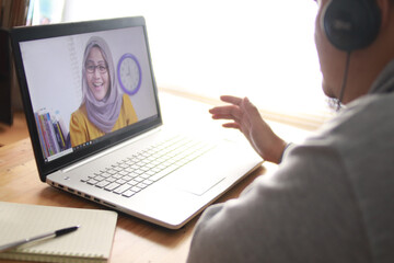 Asian man having video teleconference with a woman on his laptop at home, online learning or working from home