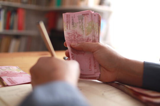 Close up of woman hand counting money uang Indonesian rupiah and making notes, money financial management