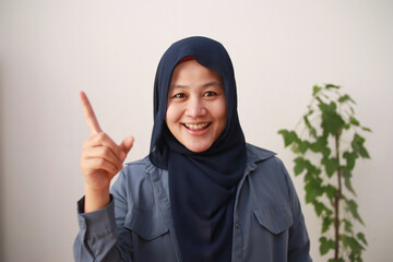 Asian muslim businesswomen wearing hijab having good idea, pointing finger up, happy smiling expression