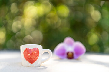 cup coffee with red heart printed against nature bokeh background.
