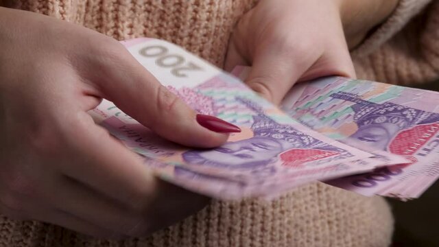 Female hands count ukrainian money hryvnia currency denomination note on pink sweater background. Business or financial concept. Money or cash revenue, finance and economy