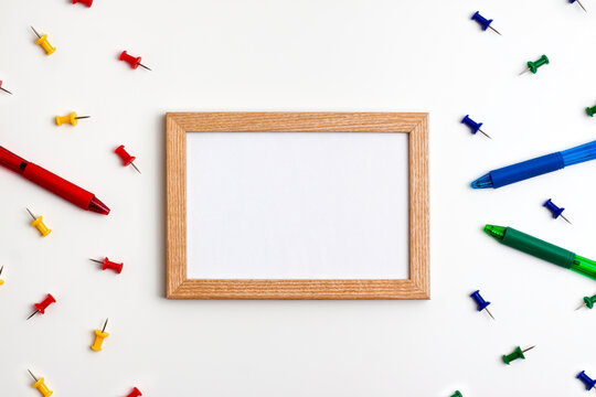 Yellow red blue green push pins, wooden frame and pens at the left and right on white background. Flat lay top view. Education back to school and online study concept