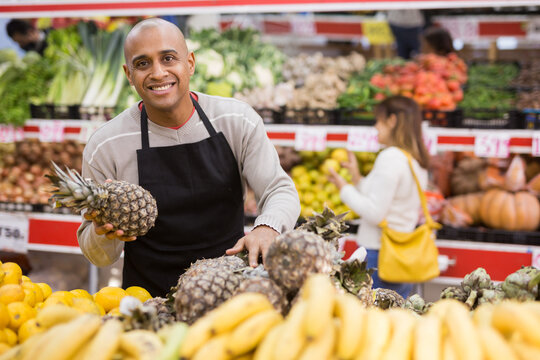 Portrait of latino-american worker in supermarket with pineapples