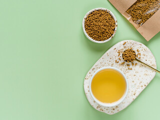 Cup of buckwheat tea on light green background. Top view of healthy soba tea and groats of tartary buckwheat seeds on green background. Flat lay. Copy space
