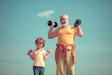 Funny old senior man and kid boy with dumbbells. Healthcare cheerful lifestyle. Active family enjoy...